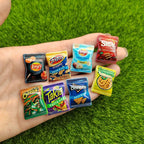 Miniature snack packs from various brands held in a hand against a grass background
