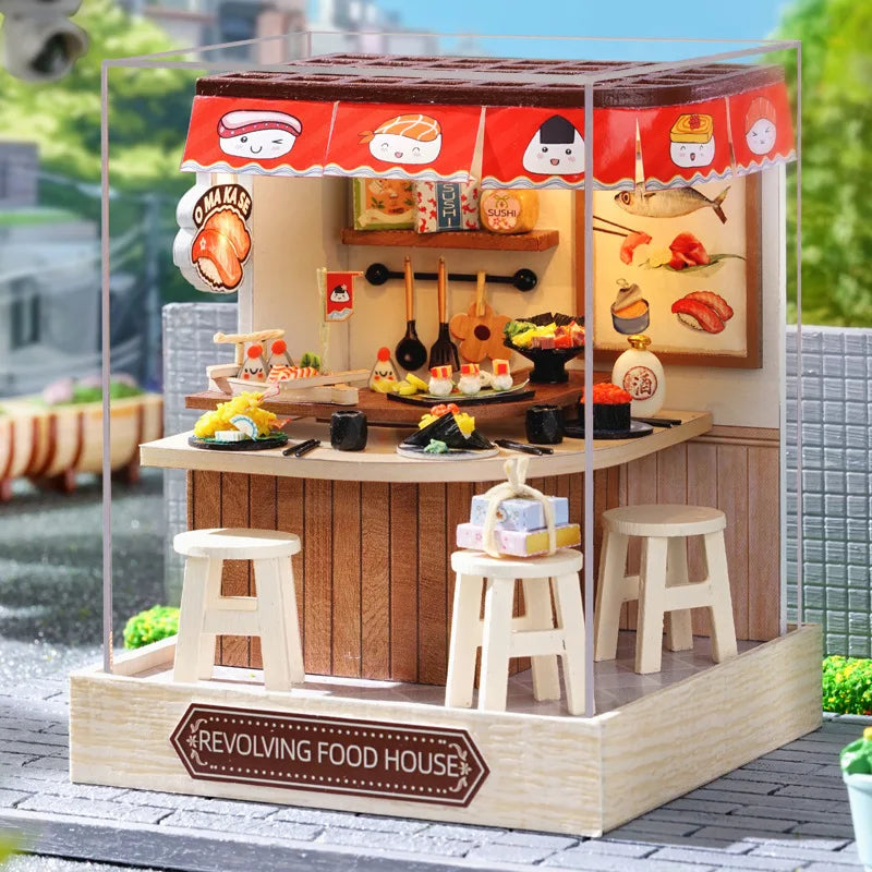 Miniature revolving food house with various food items and stools on a clear stand.
