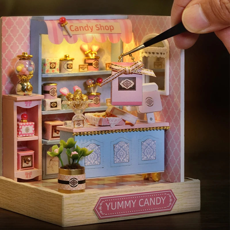 Miniature candy shop model with a hand using tweezers to place a small item inside.