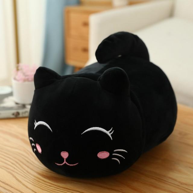 Black cat-shaped cushion with a cute face design on a wooden surface.