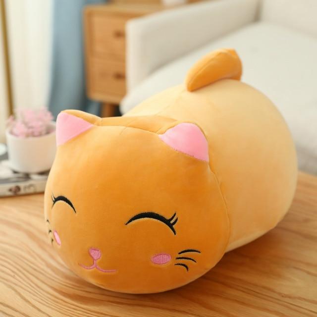Plush cat-shaped pillow on a wooden surface with a blurred indoor background