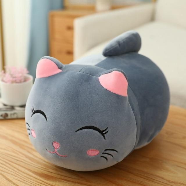 Gray cat-shaped plush toy on a wooden surface with a blurred indoor background