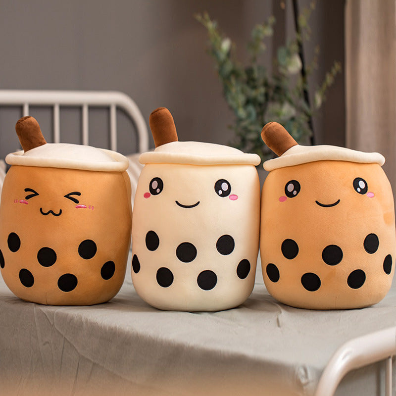 Three plush toys shaped like bubble tea cups with faces on a table.