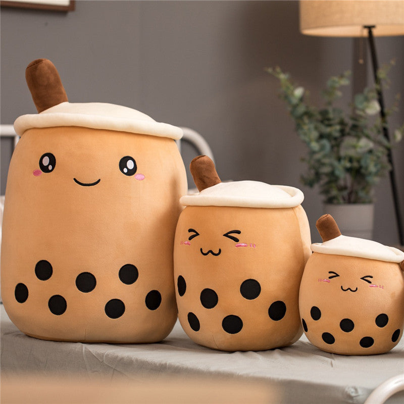 Three cute plush toys resembling bubble tea cups on a surface with a blurred background.